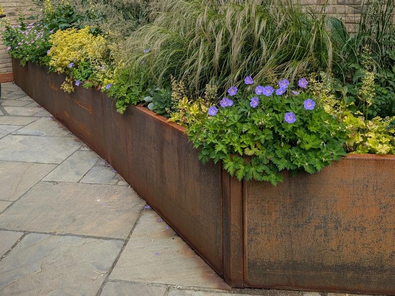 Slim profile corten steel retaining panels compared to bulky timber sleepers.